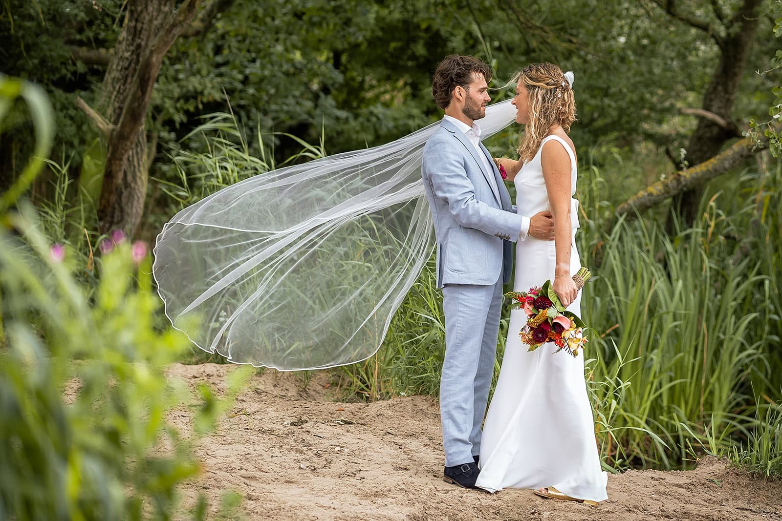 Trouwfoto van Maartje en Tim in de duinen van Zandvoort met mooie compositie sluier en groene natuur